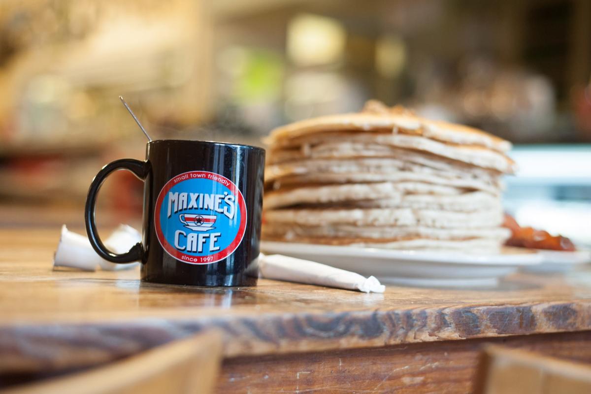 Stack of pancakes and a black Maxine’s Café coffee mug on a table in Bastrop