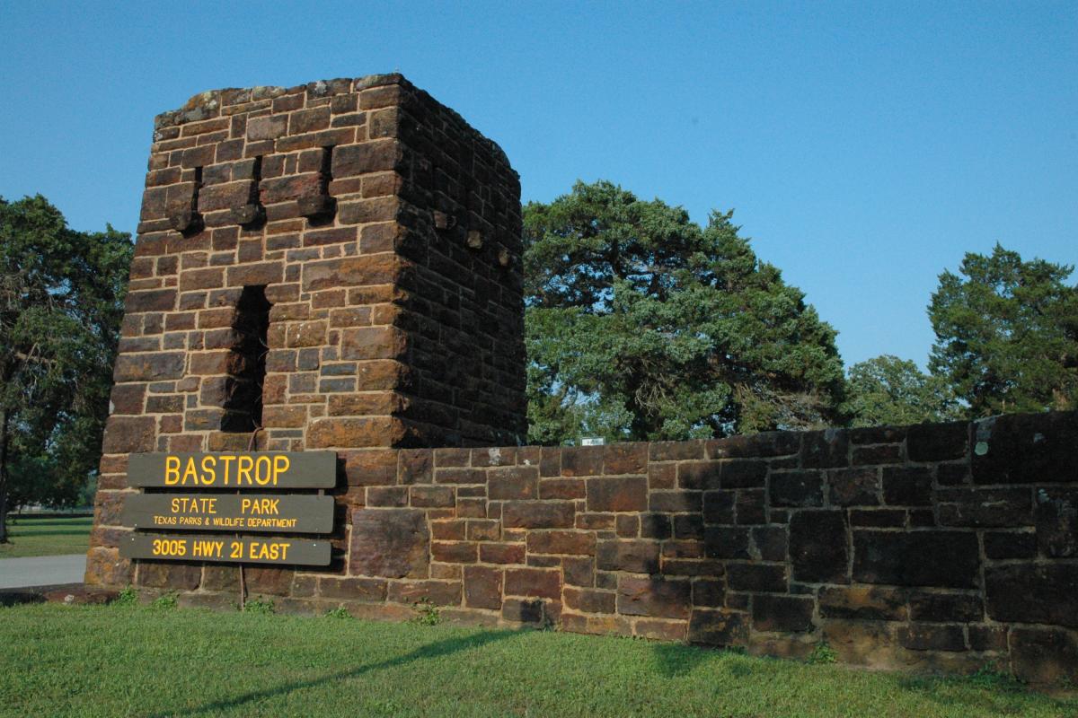 Stone entrance gateway and Bastrop State Park sign surrounded by trees