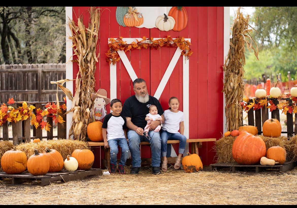 Family posing at a red barn backdrop surrounded by pumpkins at the Universal City Pumpkin Patch